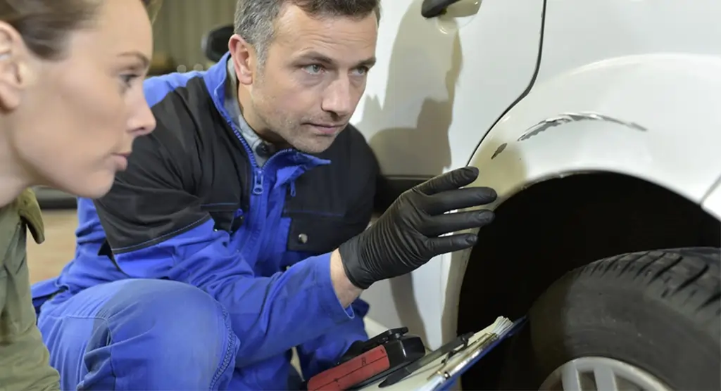 Mann im Blaumann inspiziert eine Autokarosserie auf Schäden.