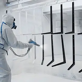 Arbeiter in Schutzanzug beim Pulverbeschichten von Metallrahmen in einer Kabine.