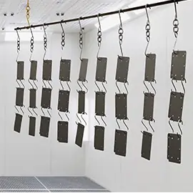 Mehrere lackierte Metallplatten hängen in einer Kabine zum Trocknen nach der Pulverbeschichtung.