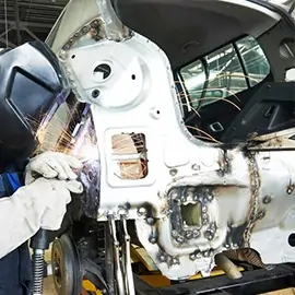Arbeiter mit Schweißmaske, der an einem Fahrzeugrahmen Schweißarbeiten durchführt.