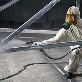 Arbeiter in Schutzkleidung, der eine große Metallstruktur mit Spritzlackierung beschichtet.